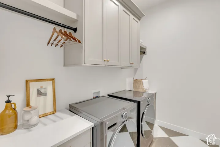 Laundry room featuring custom light-toned cabinetry, solid-surface countertops, a matte black wall-mounted clothing rod, and geometric-patterned tile flooring