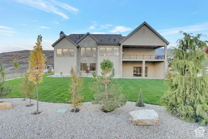 Multi-level exterior featuring stone veneer accents, stucco siding, a covered upper-level deck with black metal railing, and a covered lower-level patio