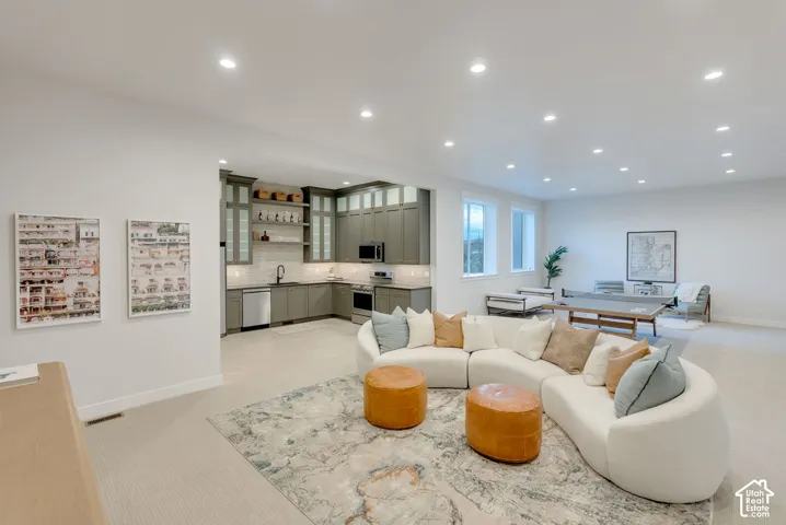 Open-concept area featuring recessed lighting, a kitchenette with grey shaker-style cabinetry, a tiled backsplash, and neutral carpeting