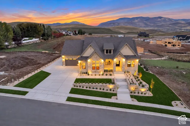 Multi-level exterior featuring stone masonry, stucco siding, a multi-gabled roofline, concrete driveway, and terraced landscaping set against a mountain backdrop
