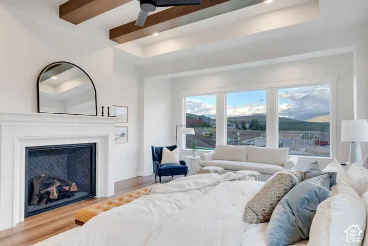 Tray ceiling with wood-finish beams, fireplace featuring a herringbone tile interior and a prominent mantel, wood-finish flooring, and expansive windows with mountain scenery