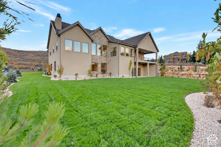 Multi-story exterior featuring a stucco facade with natural stone accents, expansive multi-pane windows, a covered balcony with iron railing, and a tiered rock retaining wall