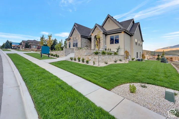 Stone and stucco exterior featuring multiple gabled rooflines, a raised stone terrace, and landscaped lawn with rock garden beds
