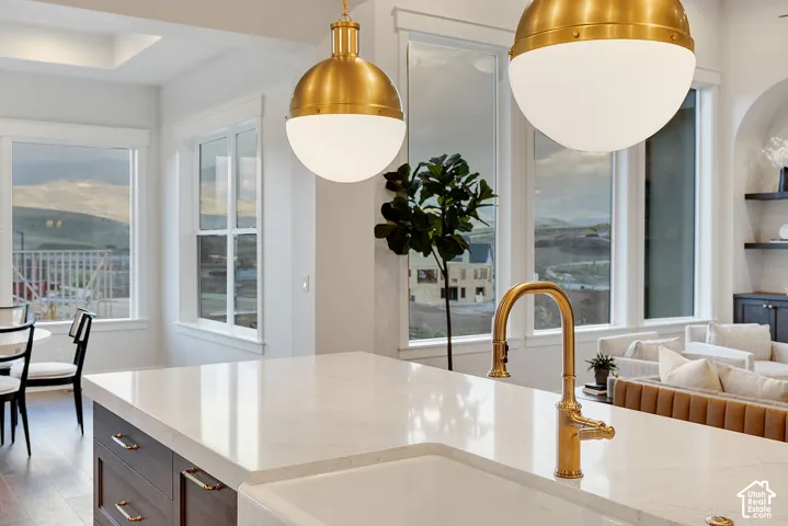 Kitchen island featuring a white stone countertop, undermount farmhouse-style sink, brass gooseneck faucet, brass globe pendant lighting, and dark-finish cabinetry
