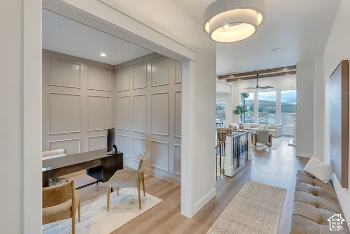 Interior featuring walls with applied wainscoting, wood-finish flooring, a tiered circular drum pendant light, a recessed ceiling, and exposed ceiling beams