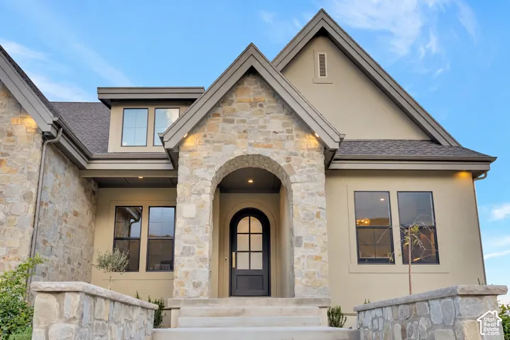 Exterior facade featuring multi-gabled rooflines, stone masonry accents, a stucco finish, and an arched entry with a glass-paneled door