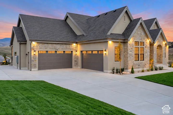 Multi-gabled exterior featuring stone veneer accents, stucco siding, a three-car garage, and an expansive concrete driveway