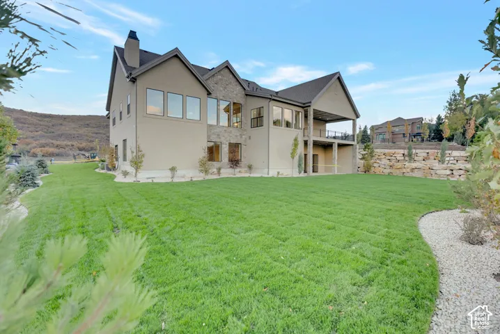 Stucco and stone exterior featuring a multi-level deck, expansive lawn, stacked stone retaining wall, and large picture windows