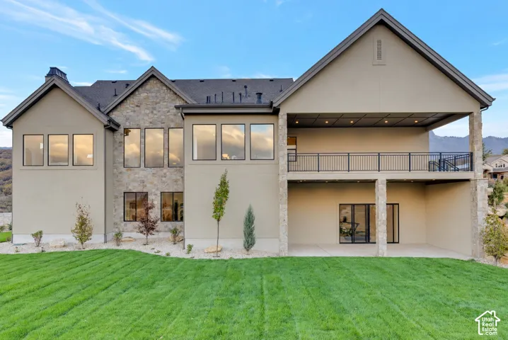 Multi-story exterior featuring a stucco and stone facade, expansive upper-level covered balcony with metal railings, ground-level covered patio, and large-format multi-pane windows