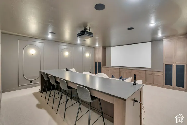 Media room featuring wall-to-wall built-in cabinetry, arched wall molding with integrated sconce lighting, ceiling-mounted projector, and a custom built-in service bar with a matte countertop