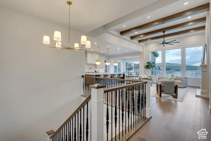 Open-concept interior featuring wood-finish flooring, exposed ceiling beams, a multi-light brass chandelier, and a custom staircase with a white balustrade and black metal spindles