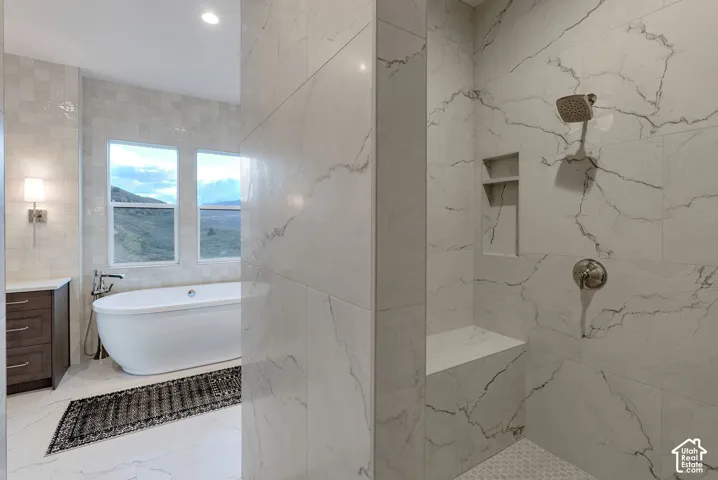 Bathroom featuring a walk-in shower with large-format tile surround, integrated bench seat, and built-in niche, paired with a freestanding soaking tub and dark-finish vanity cabinetry