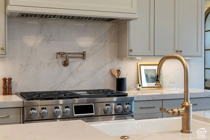 Professional kitchen featuring a stone-surface backsplash, stainless steel gas range with overhead ventilation, wall-mounted pot filler, and brass-tone hardware