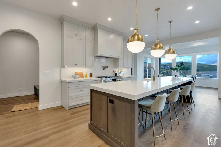 Kitchen featuring a central island with countertop seating, light-toned cabinetry, a custom range hood, pendant lighting, and wood-finish flooring