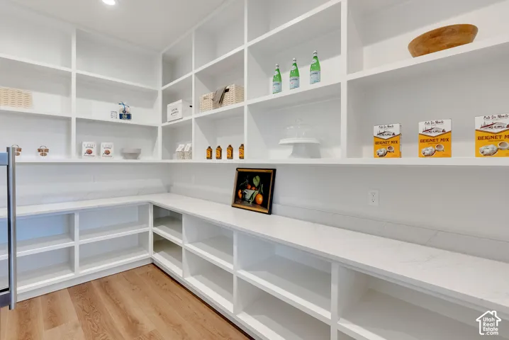 Custom walk-in pantry featuring expansive white built-in shelving, stone-composite countertops, and wood-finish flooring