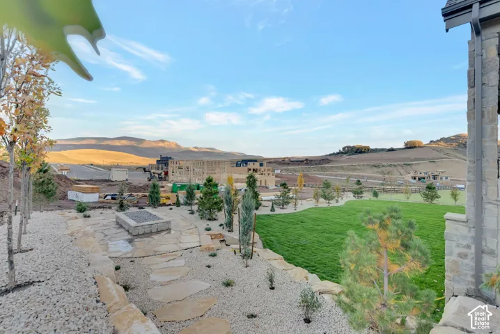 Outdoor area featuring a stone-clad fire pit, natural stone flagstone patio, manicured lawn, tiered stone retaining walls, and planted evergreens