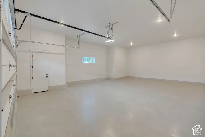 Spacious multi-car garage featuring finished walls, recessed lighting, epoxy-coated flooring, and a dedicated side-entry door