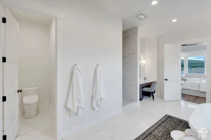 Bathroom featuring large-format tile flooring with veining, a dedicated vanity area with a stone-surfaced countertop, a walk-in shower with floor-to-ceiling decorative tile, and a separate enclosed water closet