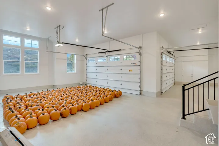 Multi-car garage featuring epoxy-coated flooring, recessed lighting, double overhead doors with inset glass panels, and a metal handrail staircase