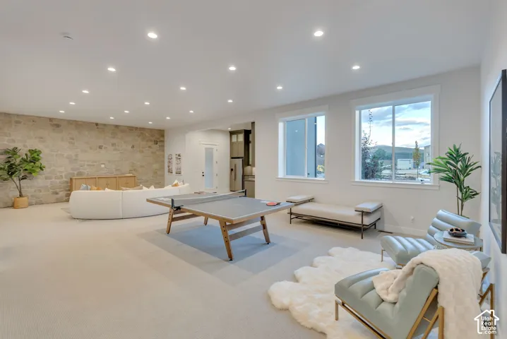 Spacious room featuring a floor-to-ceiling stone accent wall, recessed lighting, neutral carpeting, and large dual-pane windows