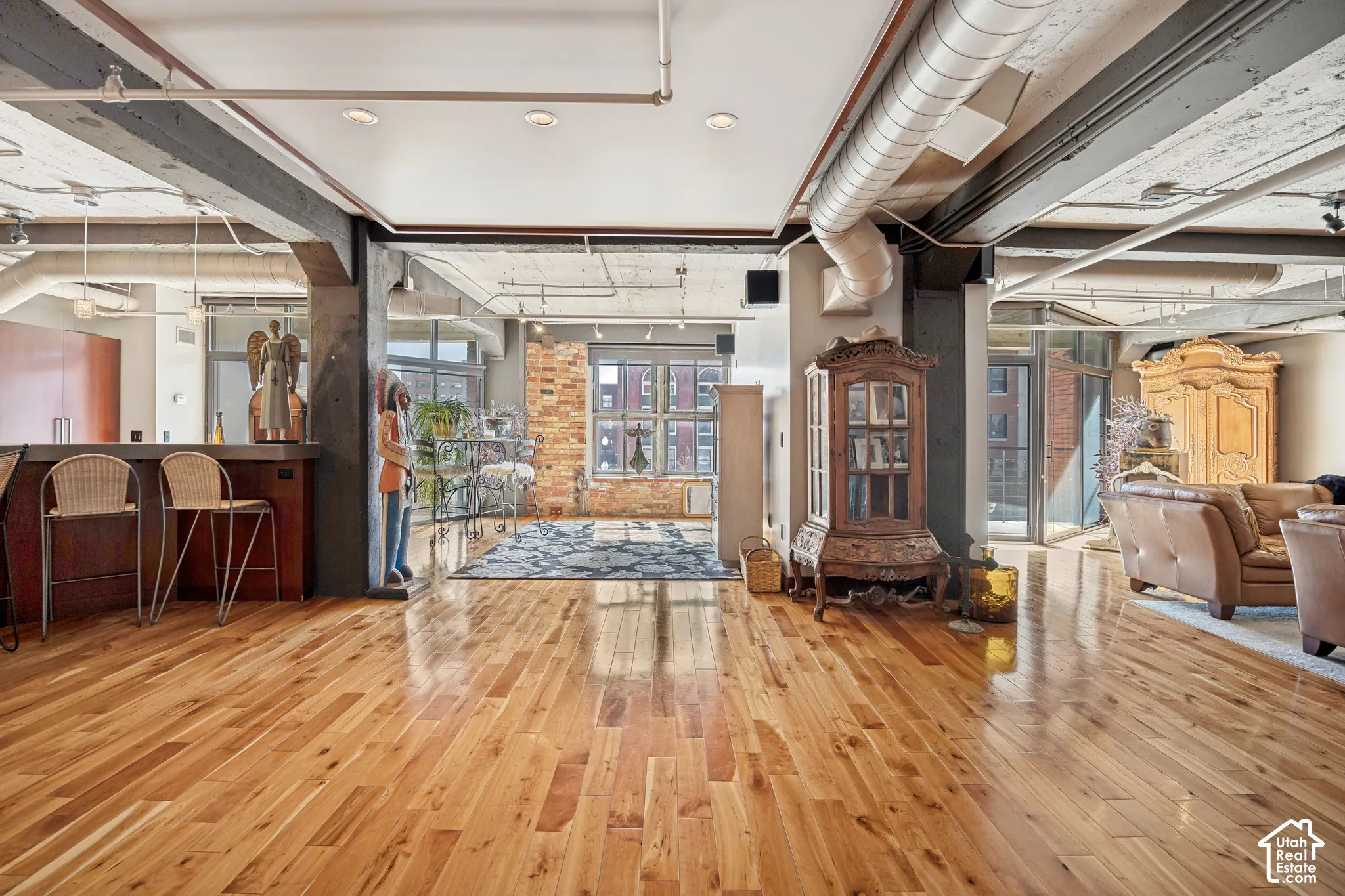 Open-concept industrial interior featuring exposed ductwork, concrete ceiling, wood-finish flooring, and exposed brick accents
