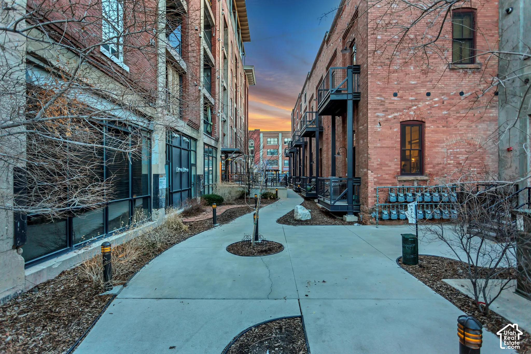 Exposed brick exterior, concrete walkway, metal balcony railings, multi-story masonry construction, and integrated ground-level glass storefronts