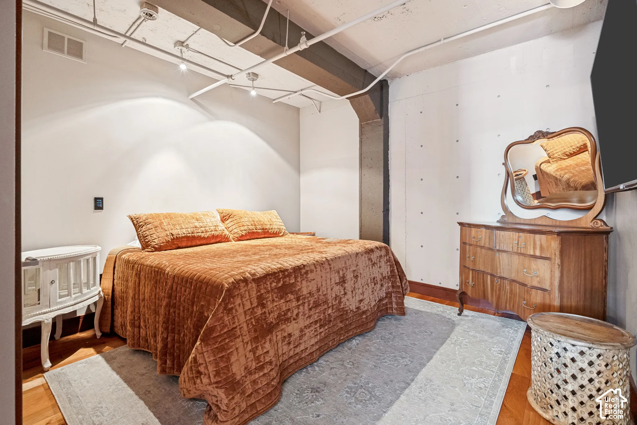Exposed concrete ceiling with industrial piping, smooth concrete wall finishes featuring structural column detail, and wood-finish flooring