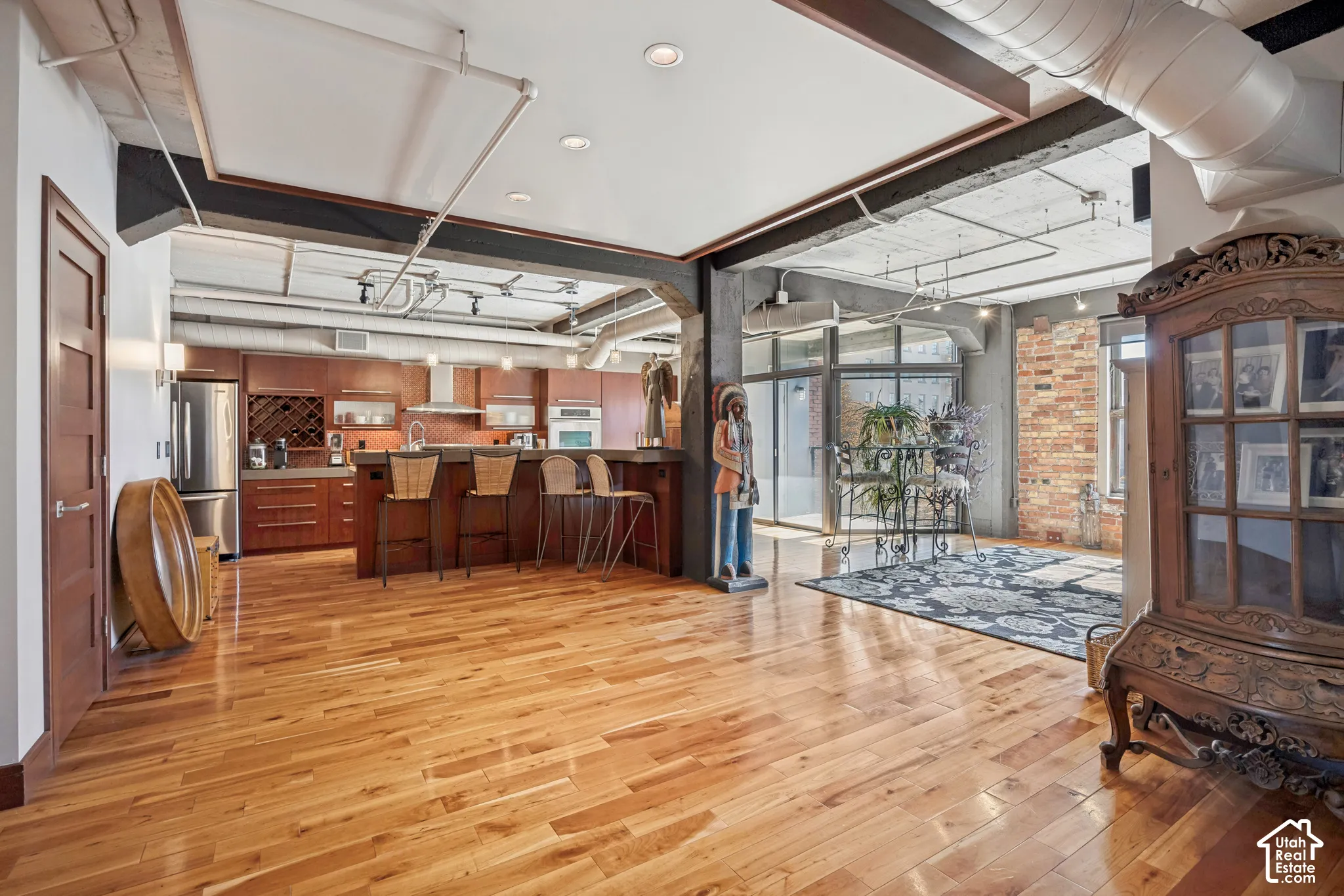 Open-concept interior featuring industrial exposed ductwork, wood-finish flooring, exposed brick wall detailing, and a kitchen island with integrated cabinetry