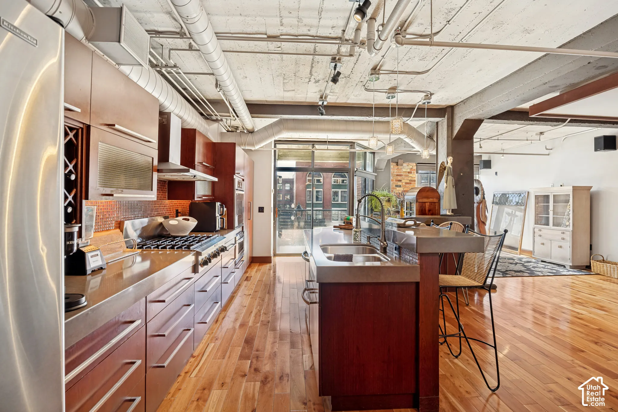 Industrial-style kitchen featuring exposed concrete ceilings and ductwork, wood-finish flooring, custom wood cabinetry, quartz countertops, and stainless steel appliances
