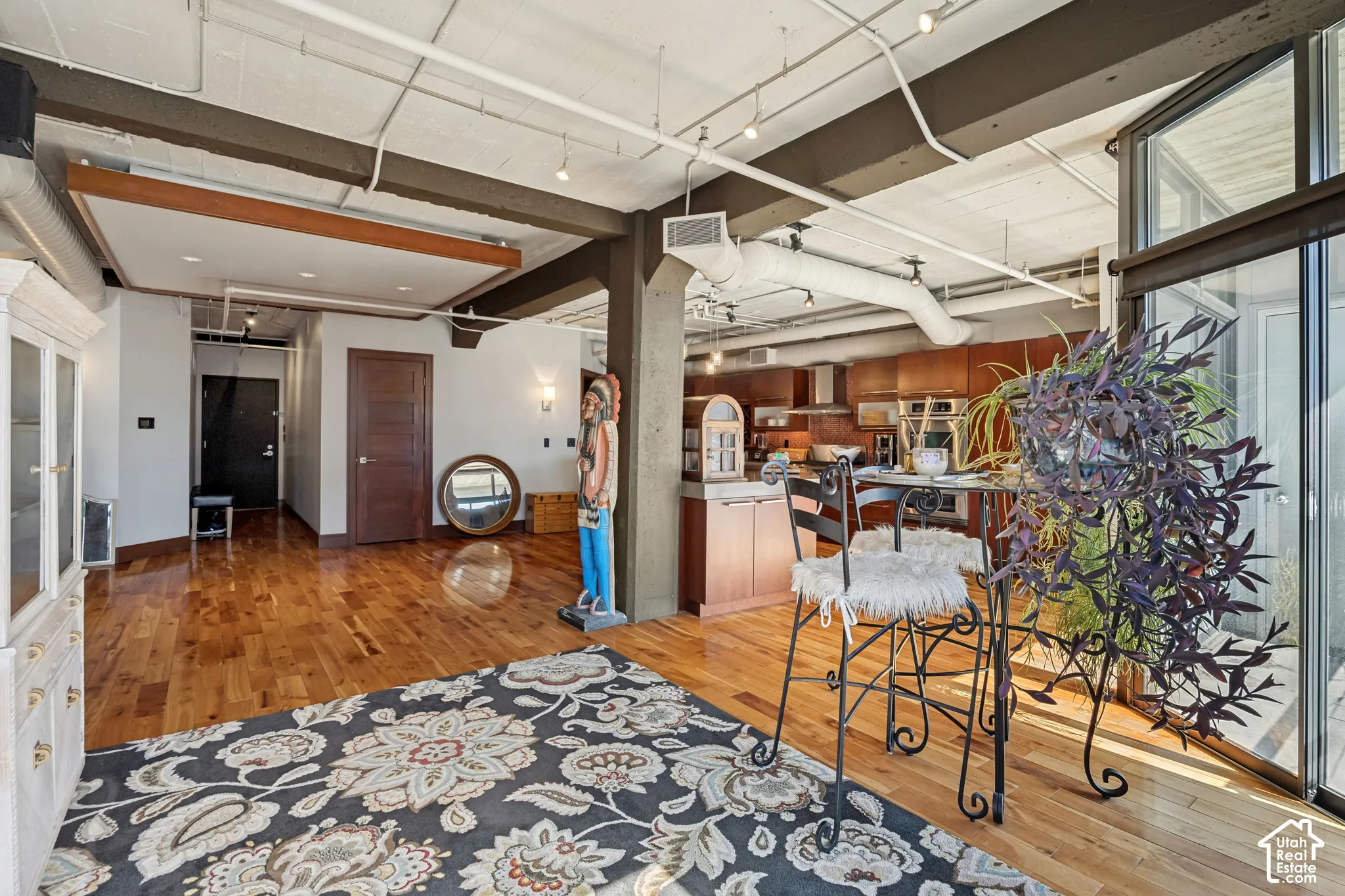Industrial-style loft featuring exposed structural beams, wood-finish flooring, track lighting, high ceilings with exposed ductwork, and floor-to-ceiling glass sliding doors