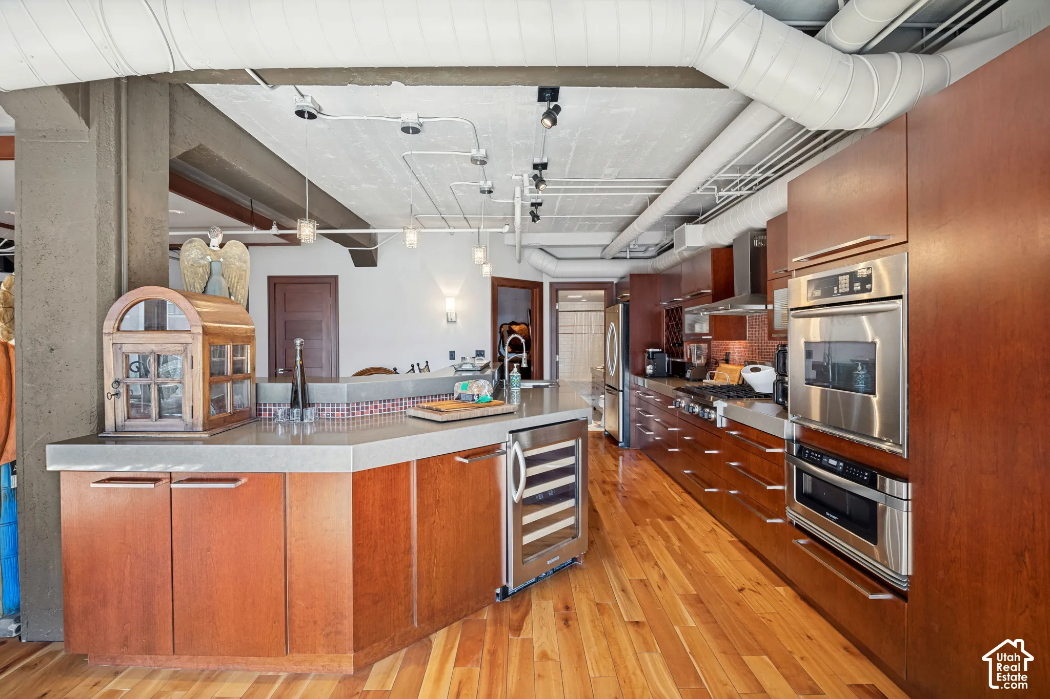 Industrial-style kitchen featuring wood-finish flooring, custom cabinetry with integrated stainless steel appliances, a built-in wine refrigerator, stone countertops, and exposed ductwork