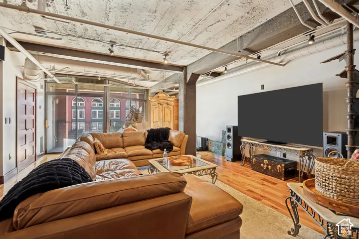 Industrial loft living space featuring exposed concrete ceilings with structural steel beams, wood-finish flooring, floor-to-ceiling glass sliding doors, and a wrought-iron spiral staircase