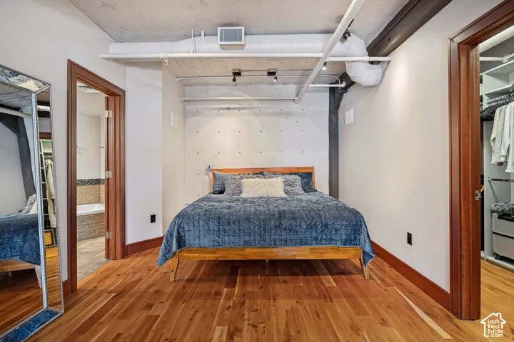 Industrial-style interior featuring exposed concrete walls, wood-finish flooring, exposed overhead ductwork, track lighting, and a built-in walk-in closet