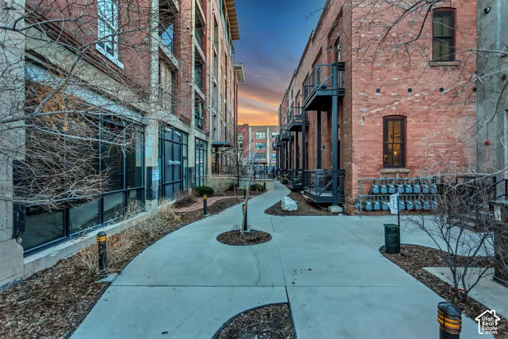 Exposed brick exterior, concrete walkway, metal balcony railings, multi-story masonry construction, and integrated ground-level glass storefronts