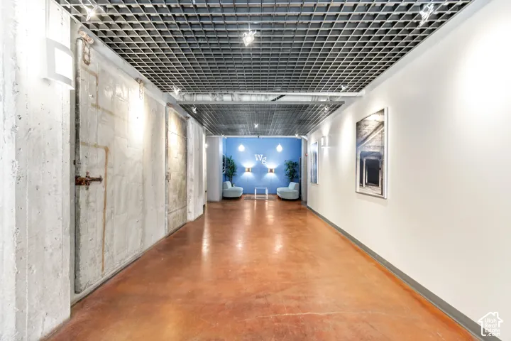 Industrial-style interior featuring a stained concrete floor, exposed concrete wall panels, a metal grid drop ceiling, and integrated wall sconce lighting