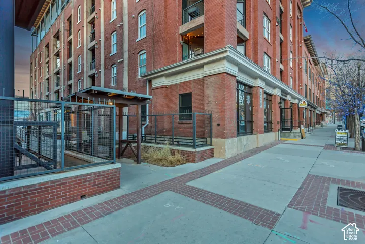 Multi-story red brick exterior featuring industrial metal balcony railings, a decorative timber-frame pergola, stone foundation accents, and extensive oversized windows