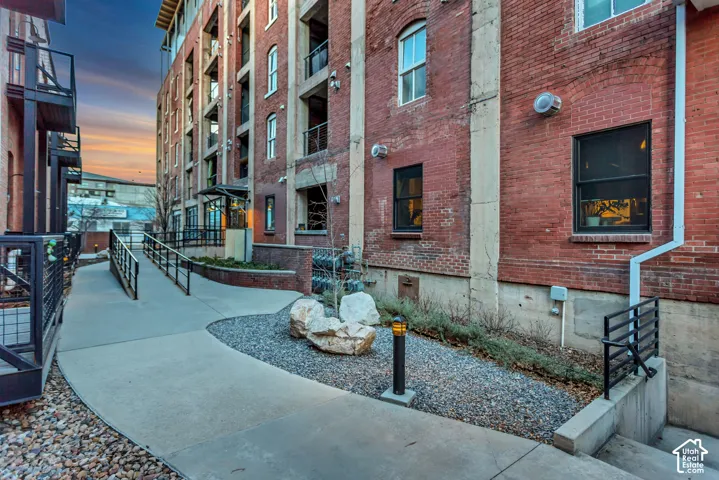 Industrial brick exterior featuring multi-story structure, concrete walkways, black metal railings, and integrated xeriscaping with decorative stone