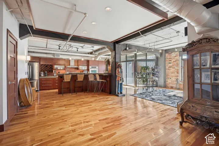 Open-concept interior featuring industrial exposed ductwork, wood-finish flooring, exposed brick wall detailing, and a kitchen island with integrated cabinetry