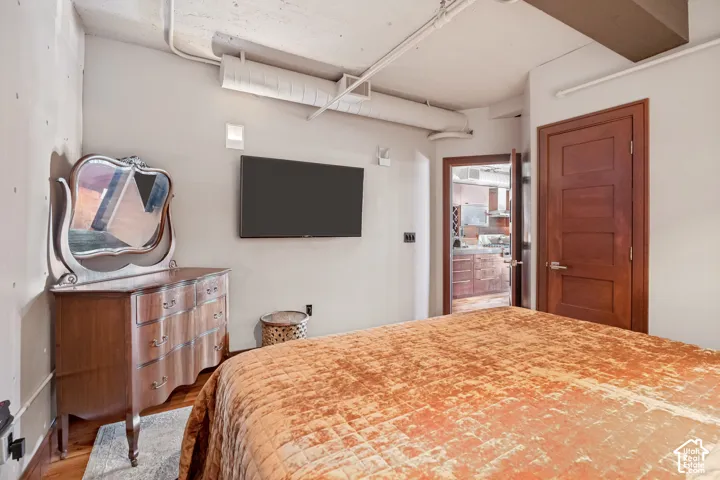 Exposed concrete ceiling with industrial-style ductwork, wood-finish flooring, and a solid wood door featuring a five-panel design