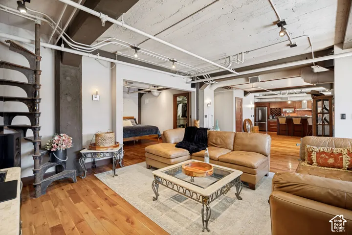 Industrial-style open floor plan featuring exposed concrete ceilings, wood-finish flooring, a custom wrought-iron spiral staircase, and exposed conduit lighting fixtures