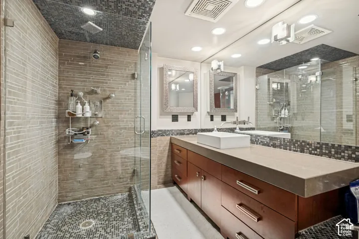 Bathroom featuring a walk-in shower with glass enclosure, horizontal tiled wall finish, and stone mosaic flooring, paired with a wood-finish vanity, solid-surface countertop, and rectangular vessel sink