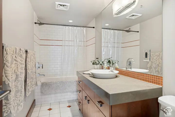 Bathroom featuring a wood-finish vanity with a stone-top counter, white vessel sink, subway tile shower surround with accent inlay, and large wall-mounted mirror