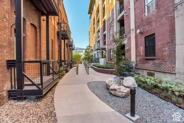 Exposed brick exterior walls, concrete walkway, metal railings, and integrated landscaping featuring gravel ground cover and boulders