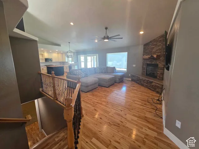 Open-concept interior featuring wood-finish flooring, a stone fireplace with a raised hearth, recessed lighting, and a staircase with a wooden handrail and iron balusters