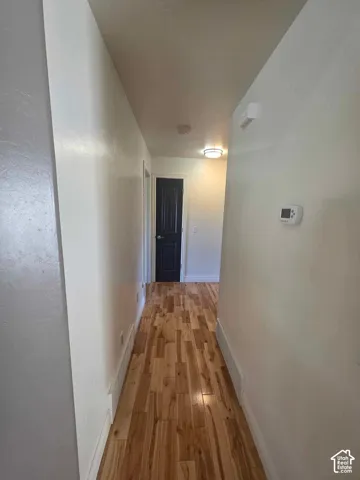 Hallway featuring wood-finish flooring, neutral wall paint, and a dark-toned interior door with architectural paneling