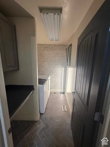 Laundry area featuring stone-finish herringbone flooring, a built-in dark countertop, and decorative brick-style wall detailing