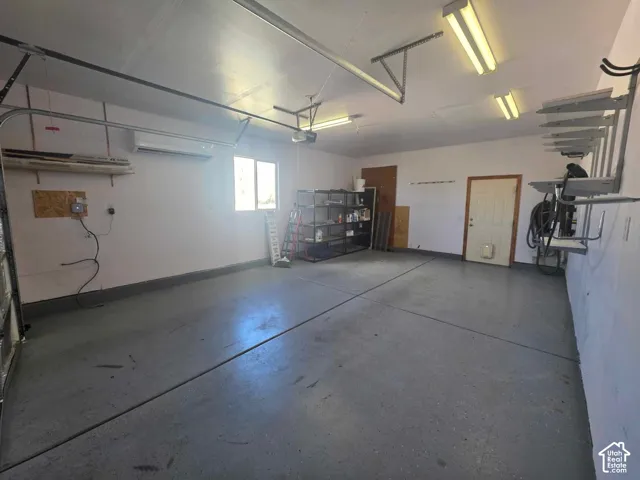 Multi-car garage featuring epoxy-coated flooring, wall-mounted climate control unit, overhead fluorescent lighting, and fixed metal wall shelving