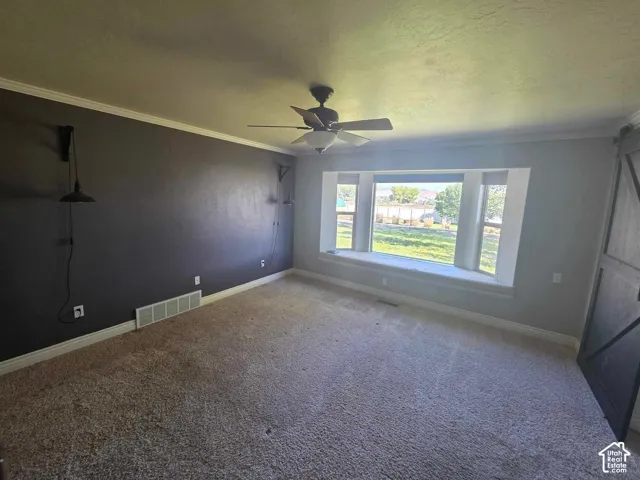 Spacious room featuring a bay window with a built-in window seat, ceiling fan, textured wall finish, and a sliding barn-style door