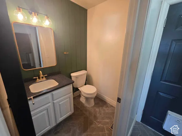 Bathroom featuring a green vertical-plank accent wall, vanity with a dark composite countertop, integrated sink with brass-finish faucet, rectangular mirror with metallic frame, and herringbone-patterned flooring