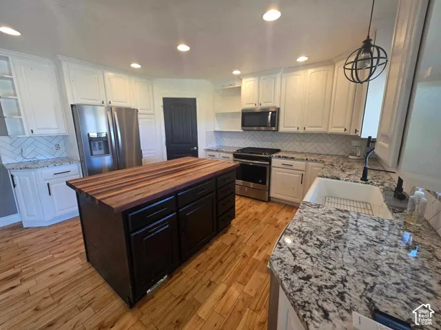 Kitchen featuring a central island with a wood-finish countertop, patterned stone-finish countertops, white cabinetry, wood-finish flooring, and a farmhouse-style apron sink